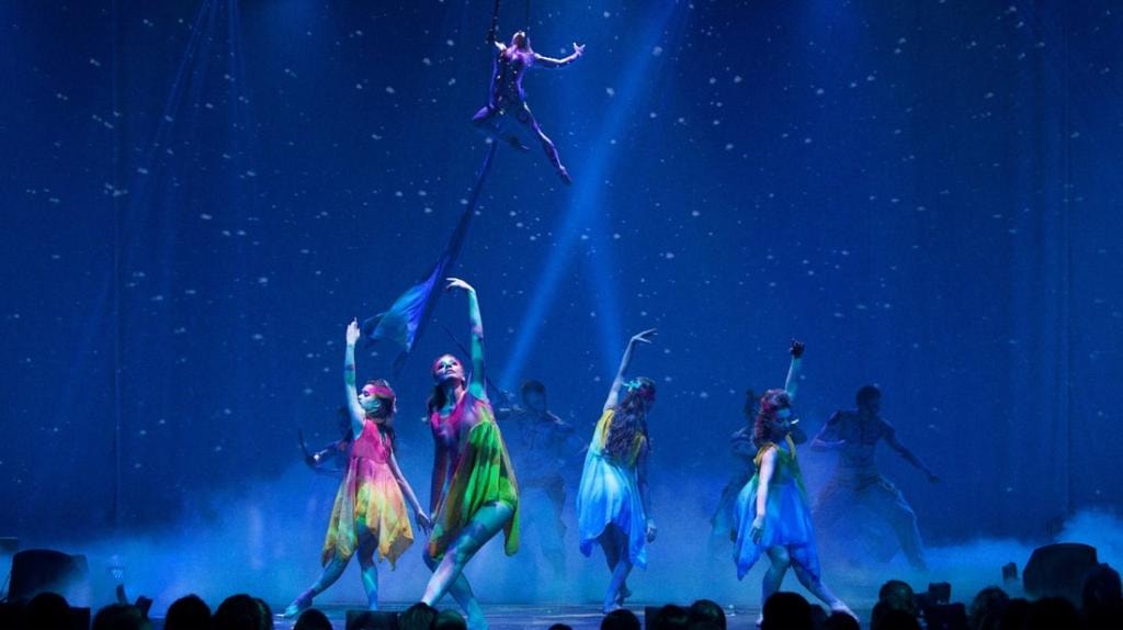 Colorful aerial and dance performance under blue stage lighting