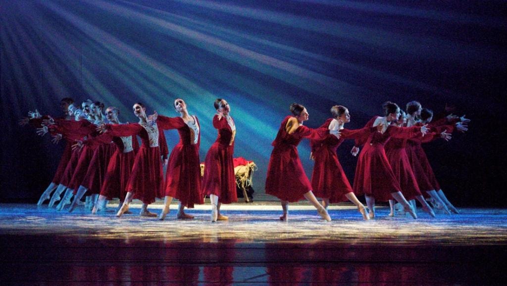 Ballet company performing in red gowns under dramatic lighting